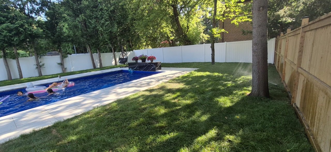 Sprinkler watering a backyard lawn next to a tree, a swing chair and a swimming pool during summer